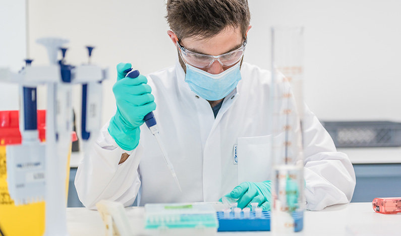 A laboratory technician using a pipette to transfer a compound to small vials.